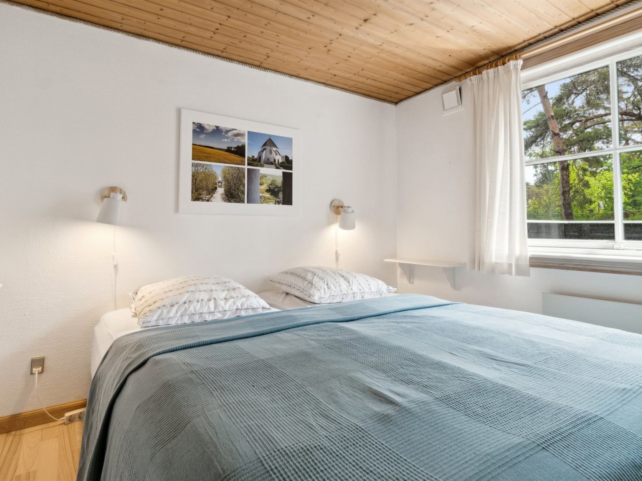 Un dormitorio con una cama, dos lámparas de noche, un ventanal con cortinas y un cuadro colgado en la pared.