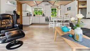 A modern kitchen with white cabinets, a black leather chair, and a dining area with white chairs and a table. - "Horsten" - 270m from the sea by Interhome (Nexø)