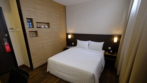 A hotel room with a large bed, wooden panel wall, bedside tables with lamps, and a small shelf with toiletries. - The Corner House (Kuala Belait)