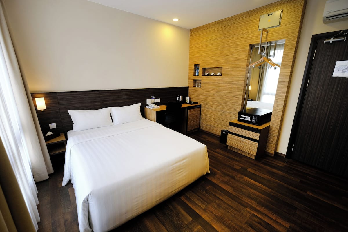 Quarto de hotel com uma cama grande, cabeceira de madeira, escrivaninha com cadeira, espelho e guarda-roupa.