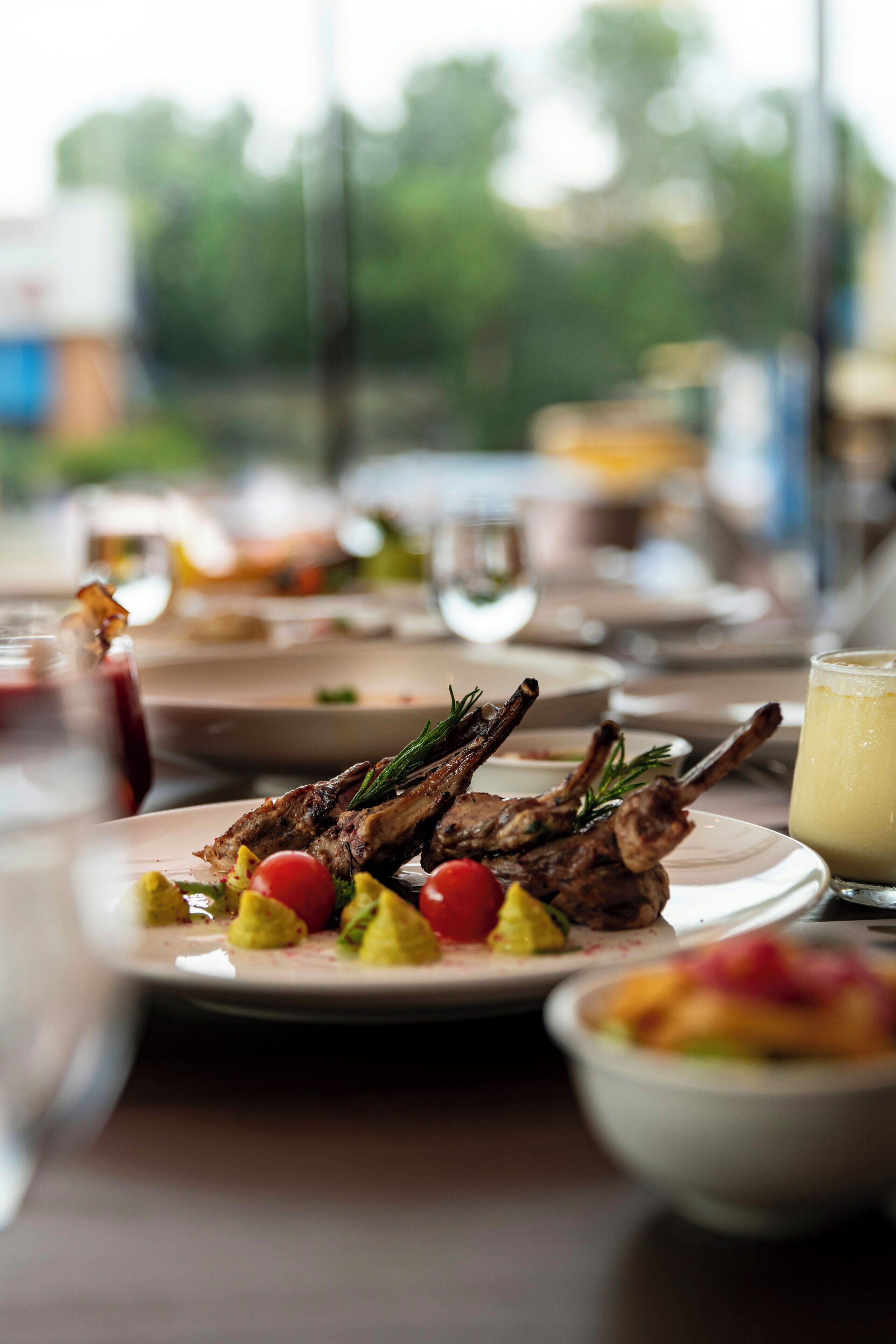 A dining table with plates of food, including roasted lamb chops and vegetables.