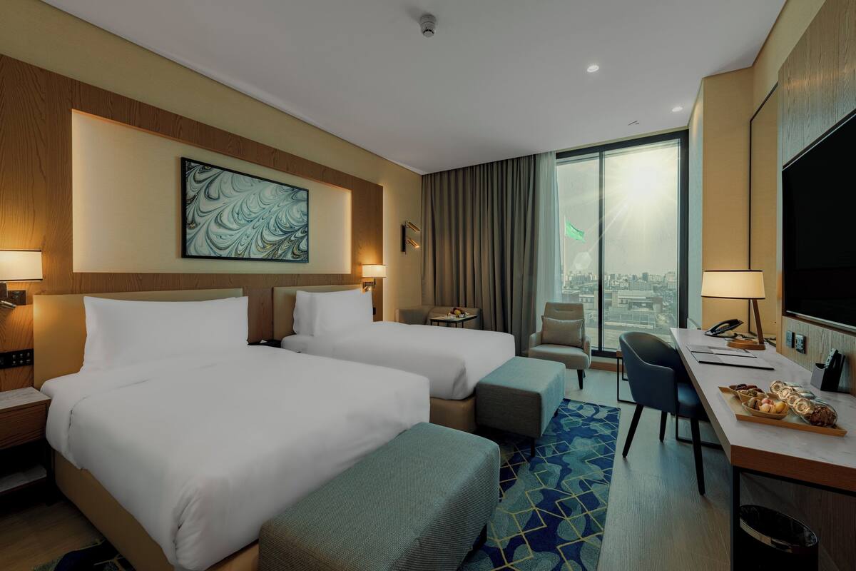 A hotel room with two beds, a desk with a chair, a TV, and a city view.