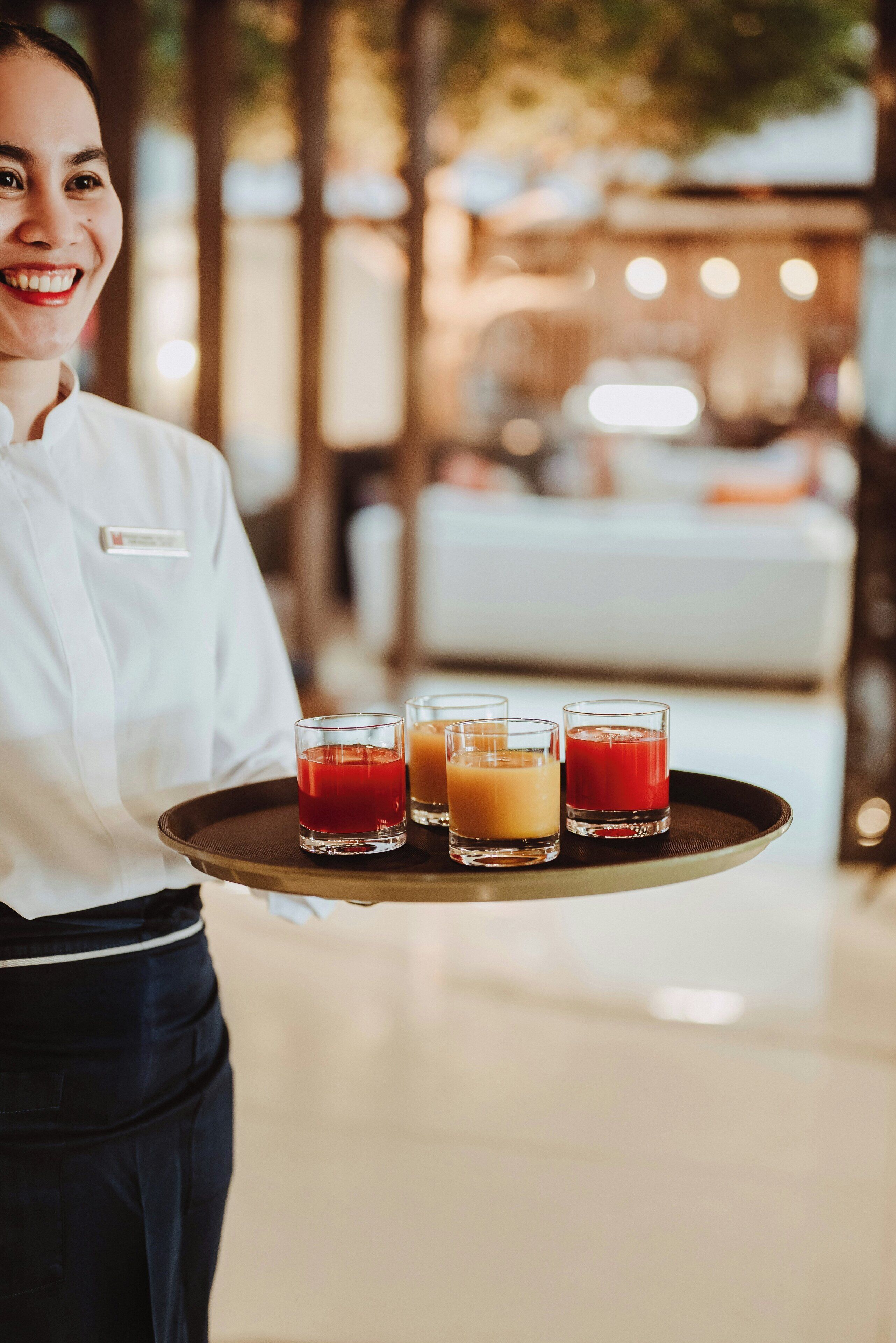 Une personne tenant un plateau sur lequel se trouvent trois verres de jus.