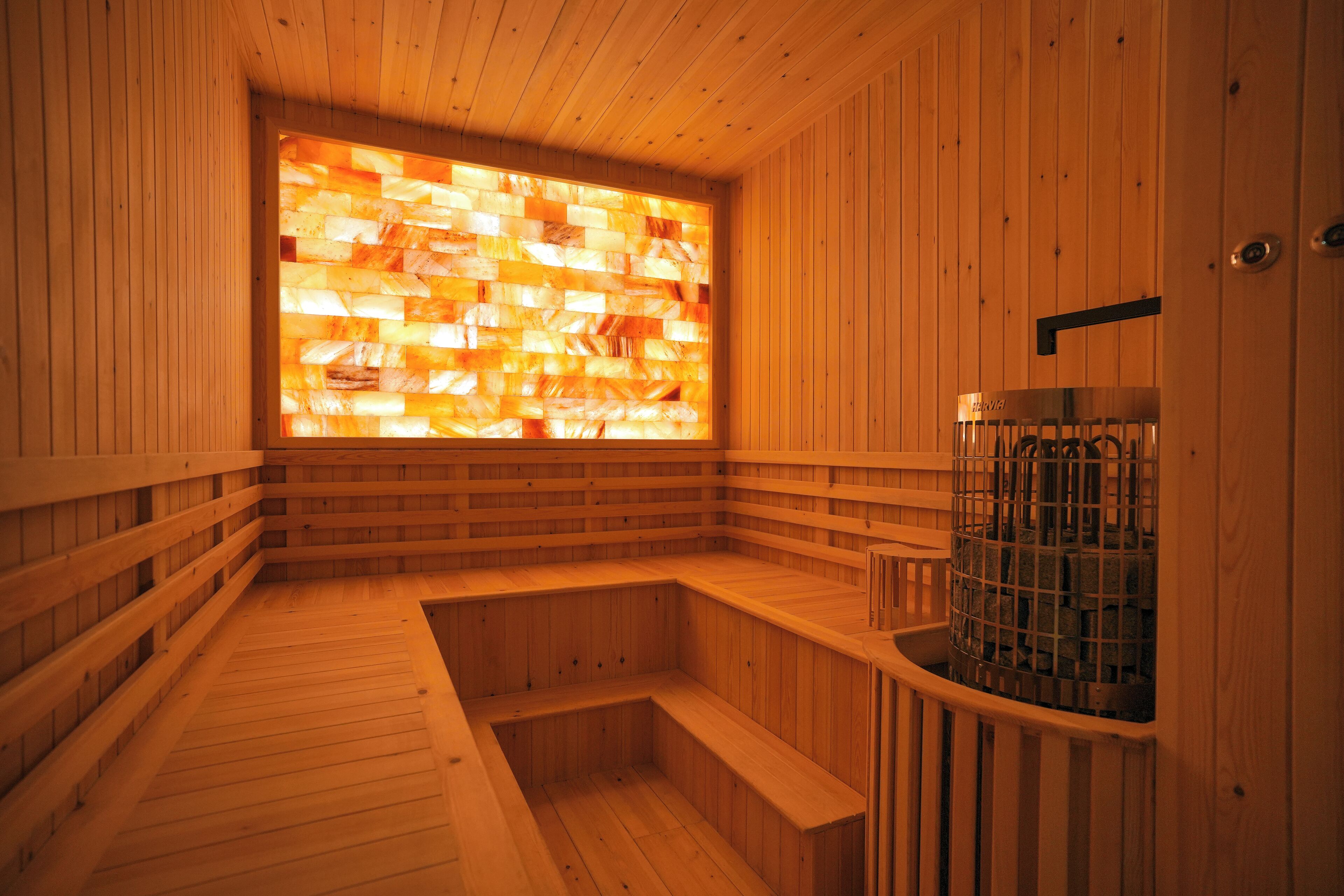 A wooden sauna with a large window, wooden benches, and a metal container.