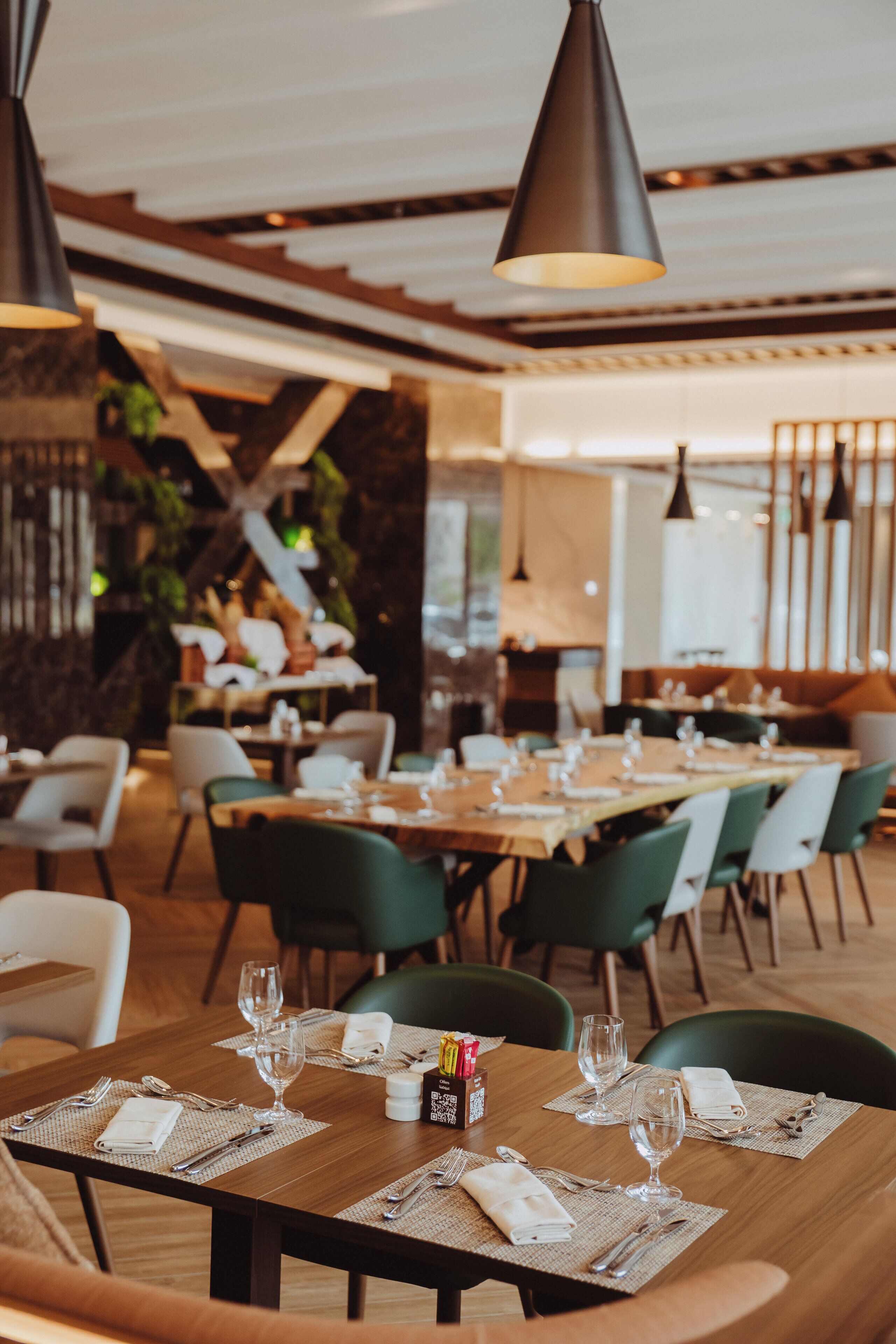 A restaurant with wooden tables and chairs, set with wine glasses and cutlery.