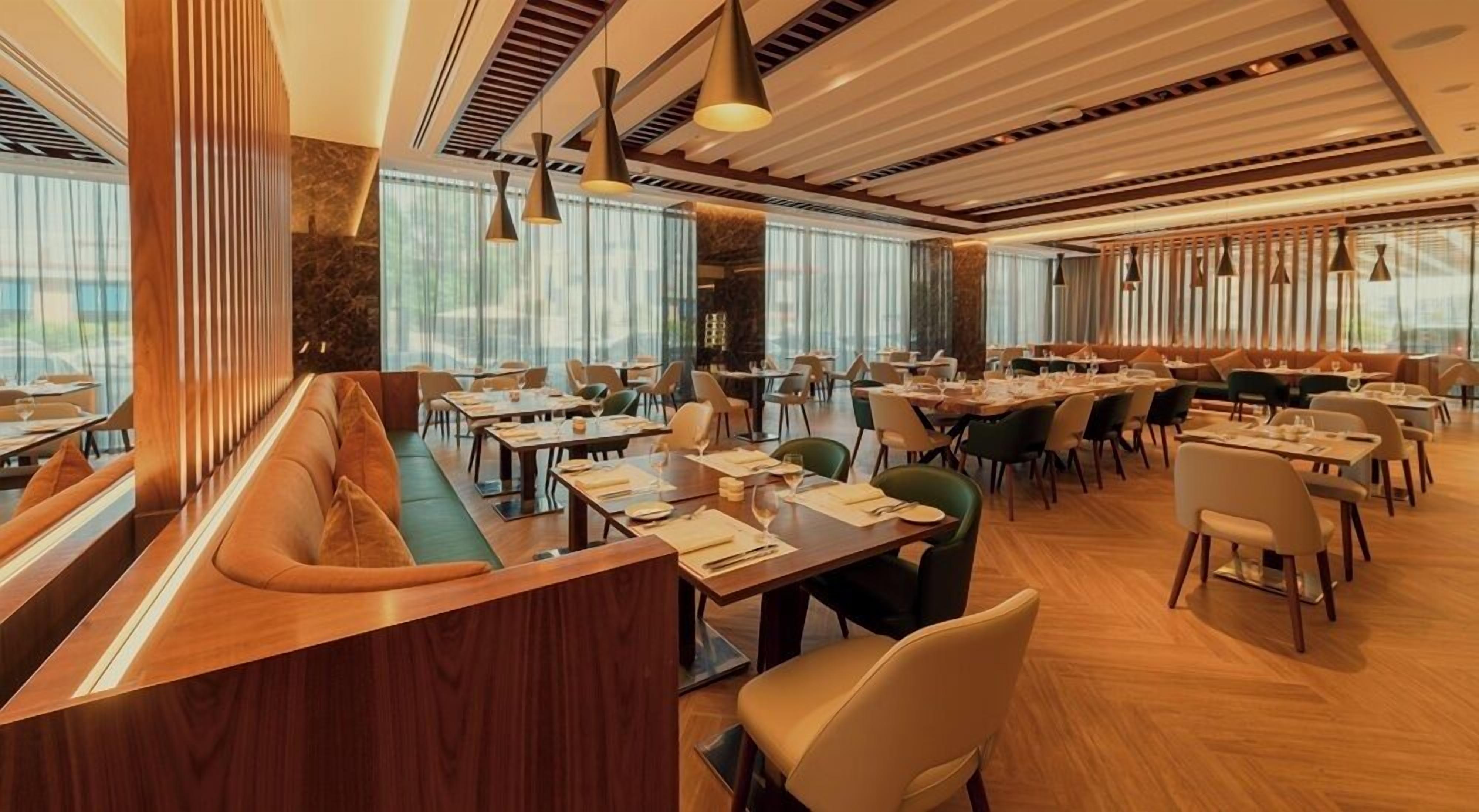 En modern restaurang med en lång bardisk, flera matbord och en blandning av sittplatser i form av bås och stolar.