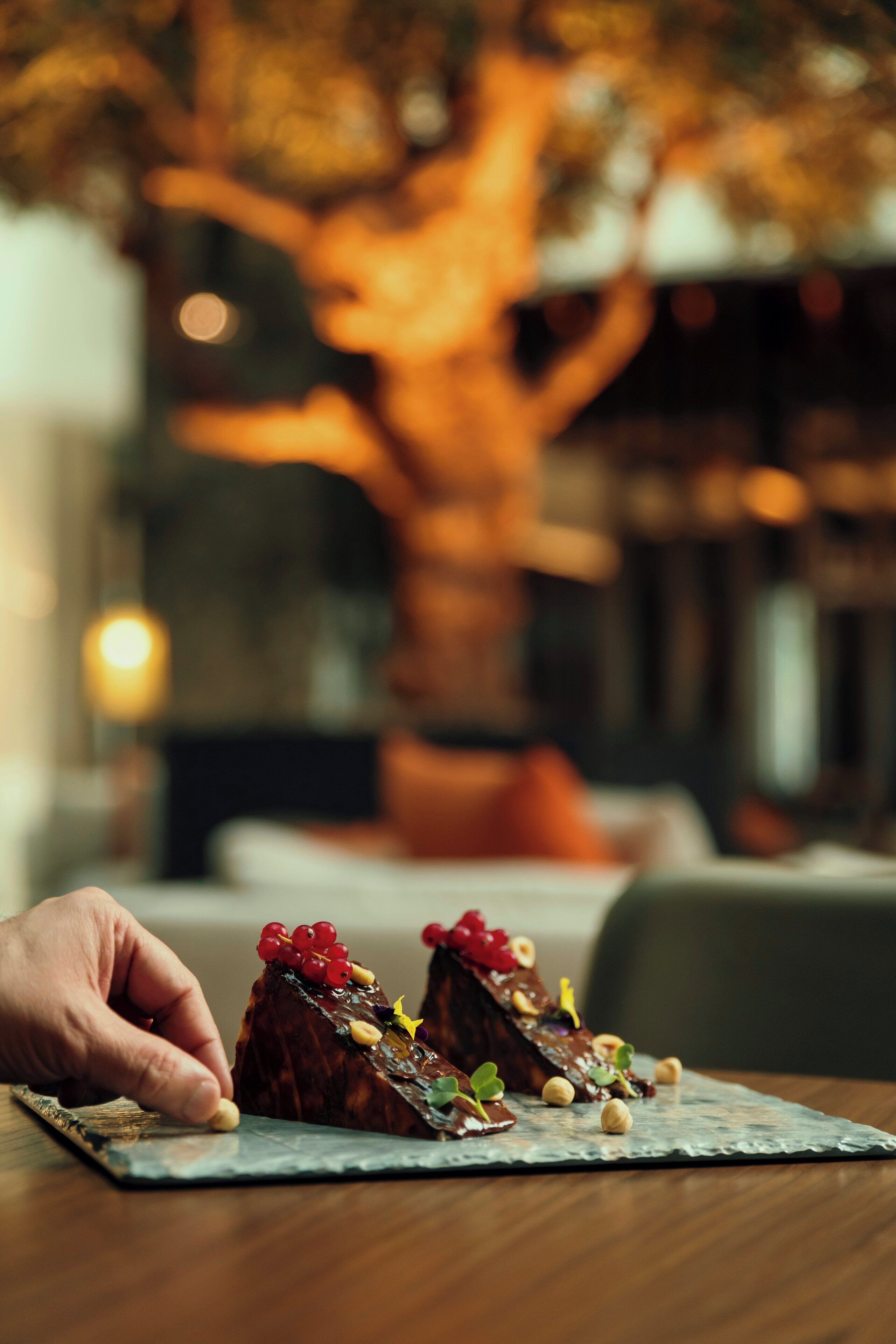 A dessert on a slate plate with a blurred background of a tree and a person.