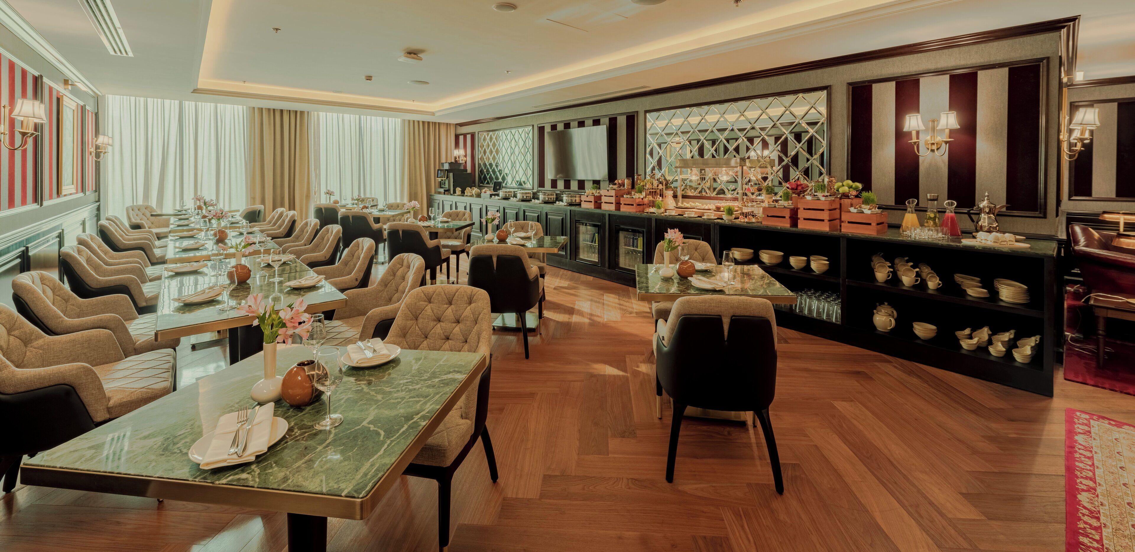 Un comedor amplio con varias mesas y sillas, una barra con estantes llenos de copas y botellas, y un ventanal con cortinas.