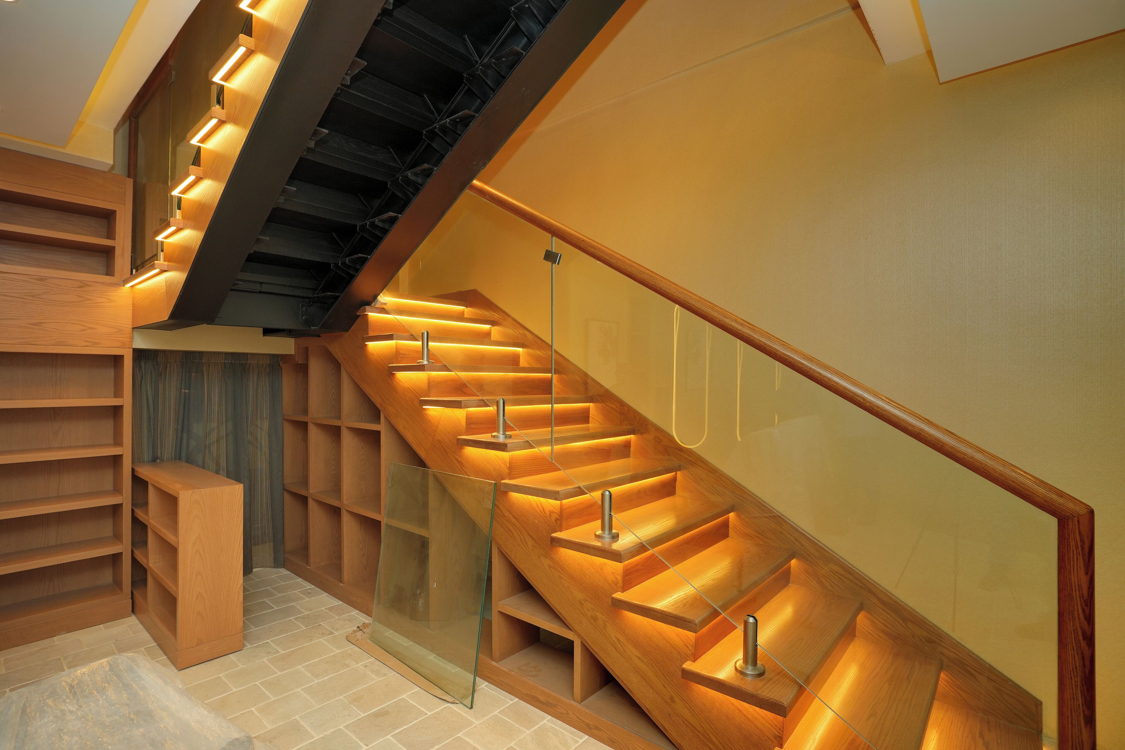 A modern staircase with wooden steps and glass railings, leading to a lower level.