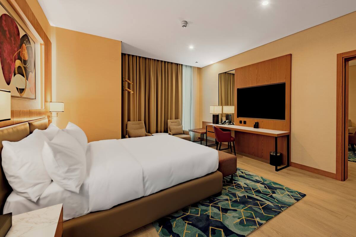 A hotel room with a large bed, a desk, a chair, a TV, and a mirror.