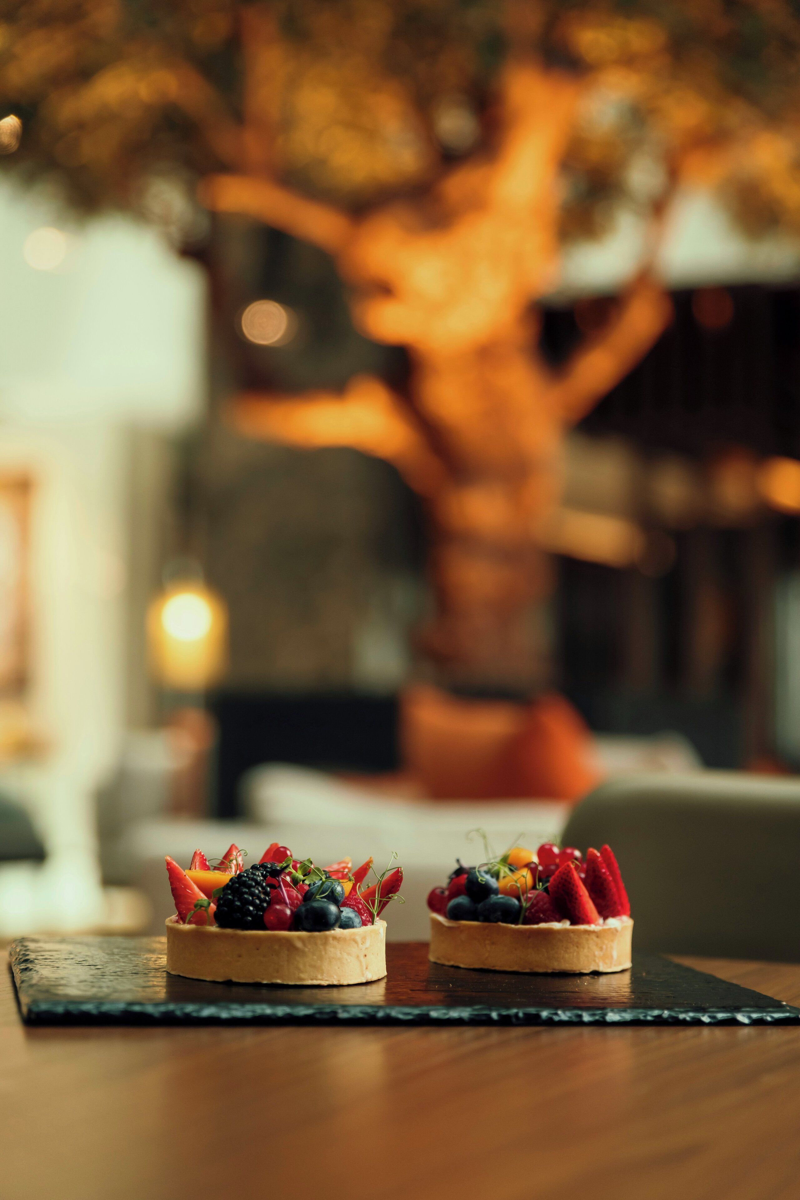 Dos tartas de fruta sobre una mesa de madera con un fondo desenfocado que muestra un árbol y una lámpara.