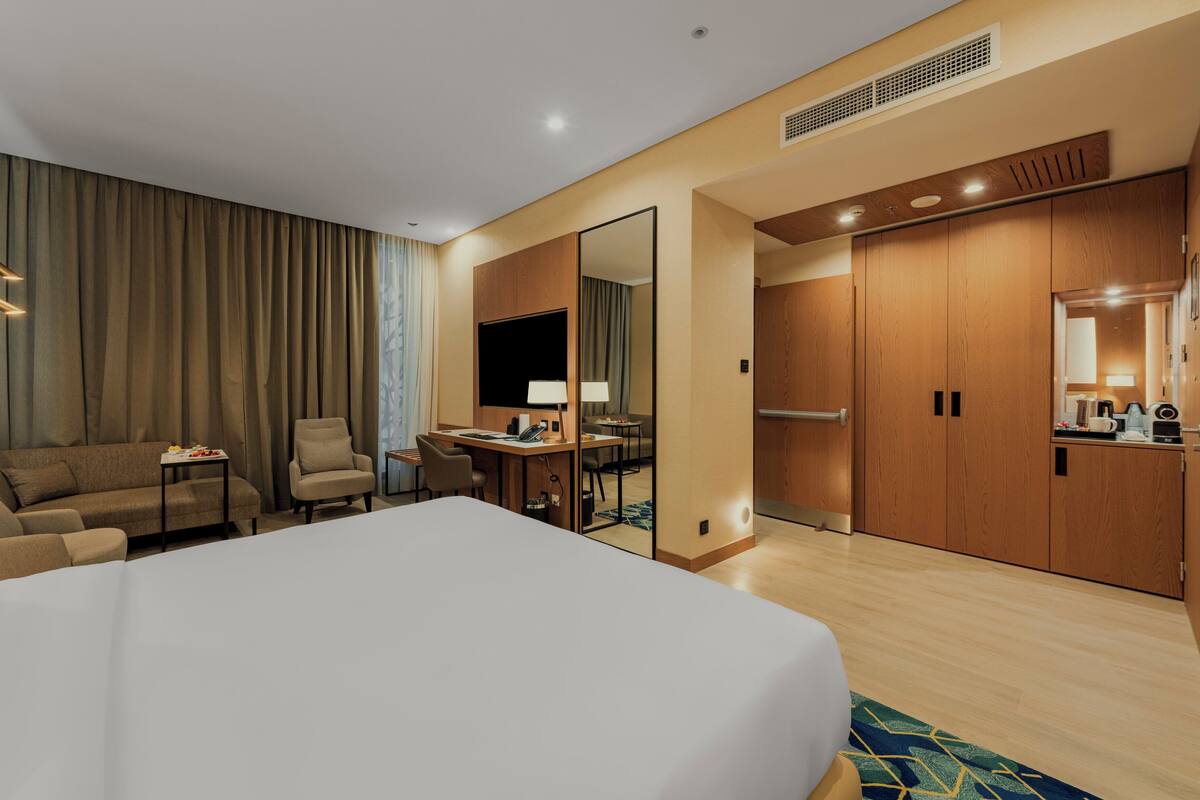 A hotel room with a large bed, a desk with a chair, a sofa, a TV, and a wardrobe.