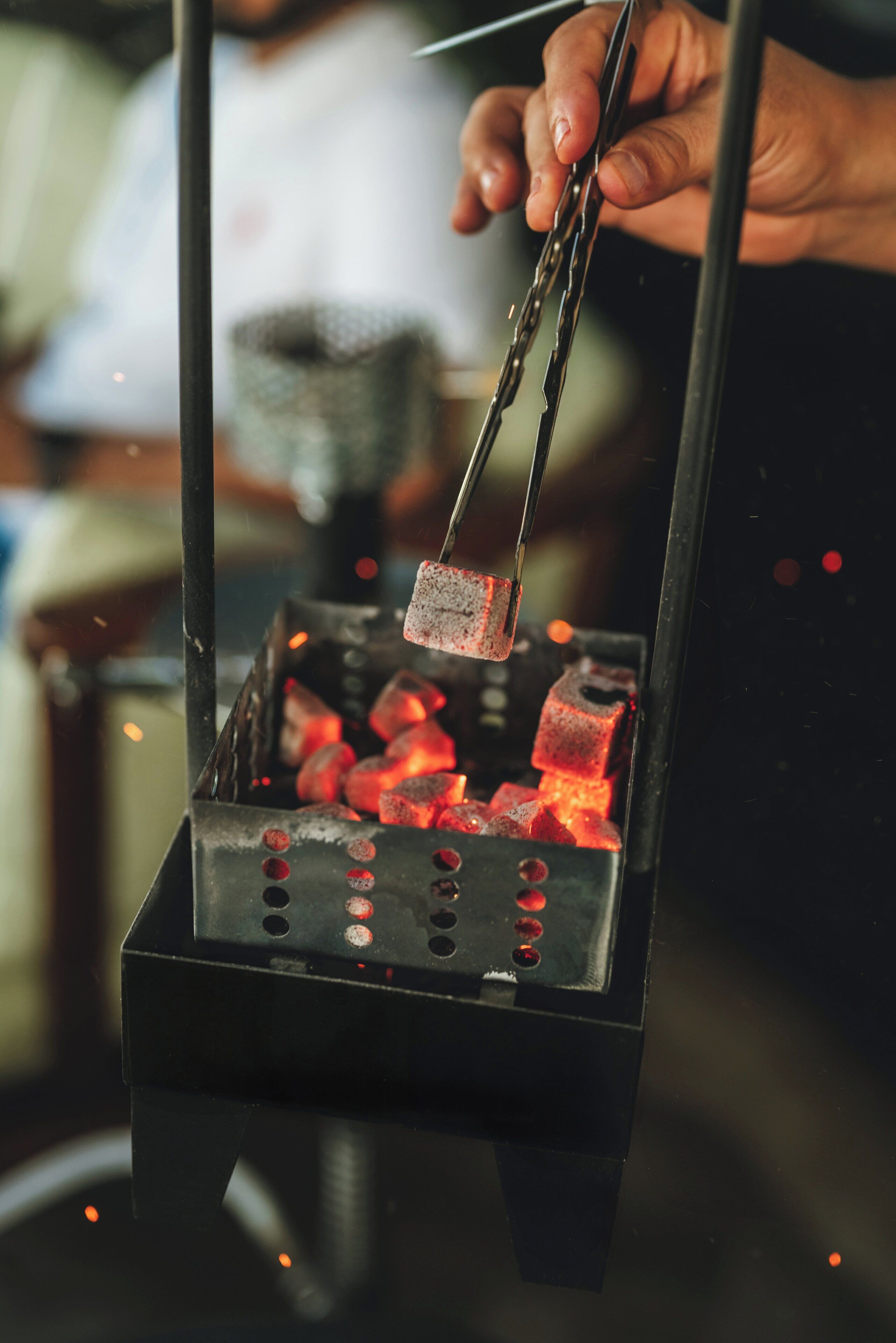 A person using tongs to handle a piece of food over a grill with visible charcoal.
