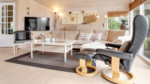 A modern living room with a wooden ceiling, a large flat-screen TV, a sofa, a coffee table, and a black leather chair.