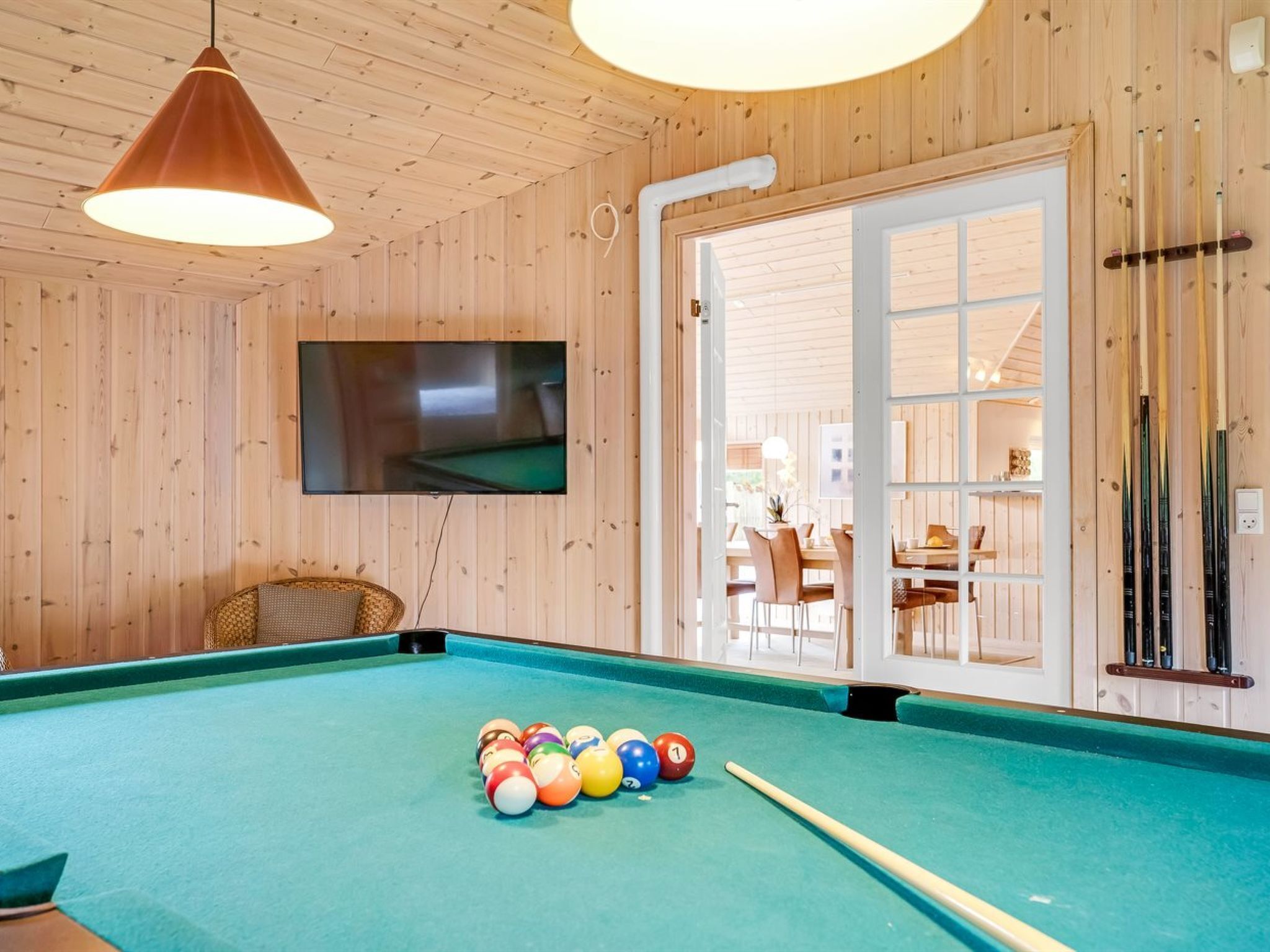 A pool table with balls, a television, and a door leading to a dining area.
