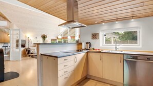 A modern kitchen with wooden ceiling beams, a central island with drawers, a built-in oven, and a dishwasher.