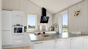Une cuisine moderne avec des meubles blancs, une hotte en acier inoxydable et une grande fenêtre offrant une vue sur l’extérieur.