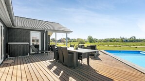 Une terrasse en bois avec une piscine, un espace salon extérieur et un coin abrité équipé d’un barbecue.