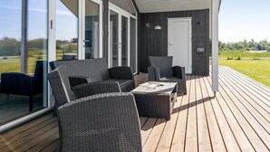 Une terrasse extérieure moderne, dotée de meubles en osier, de grandes portes-fenêtres coulissantes et offrant une vue sur la campagne.