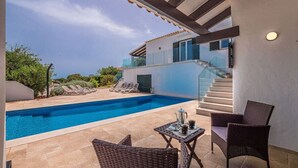 Ein Schwimmbecken mit Liegestühlen, ein Tisch mit Teekanne und eine Treppe, die zu einer zweiten Etage führt.