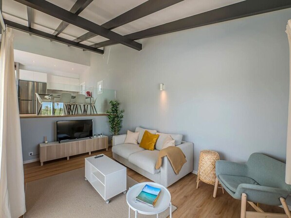 A modern living room with a sofa, coffee table, and TV. A kitchen is visible in the background. - Villaser - nice seaview and pool (Cala Llonga)