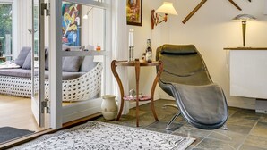 Una habitación acogedora con un sofá, una silla, una mesa con una botella y un cuadro en la pared.