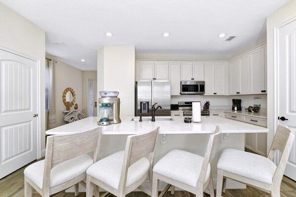 A modern kitchen with white cabinetry, a central island with seating, and a stainless steel refrigerator.
