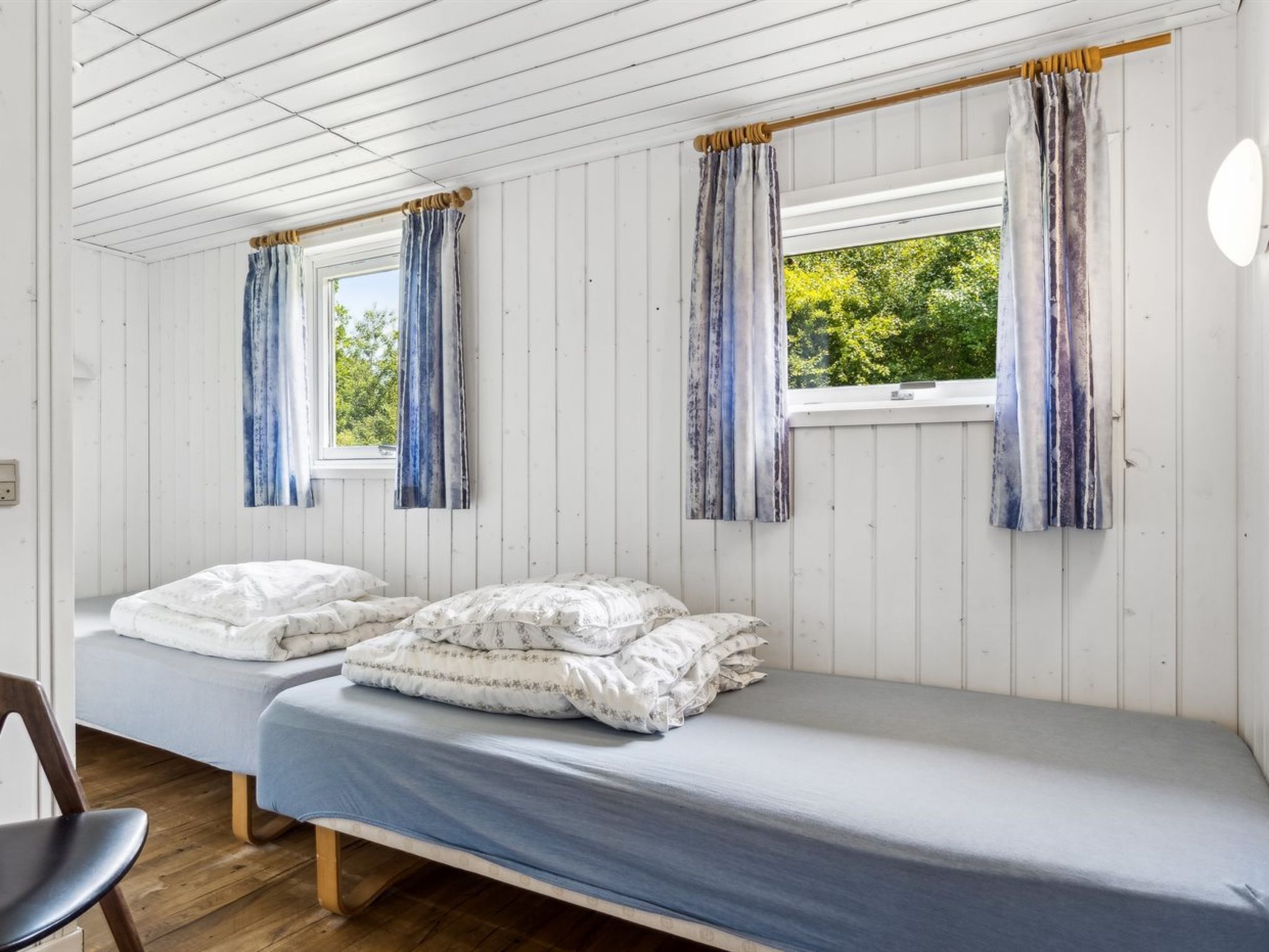 Une chambre avec deux lits simples, un plancher en bois et une fenêtre avec des rideaux.
