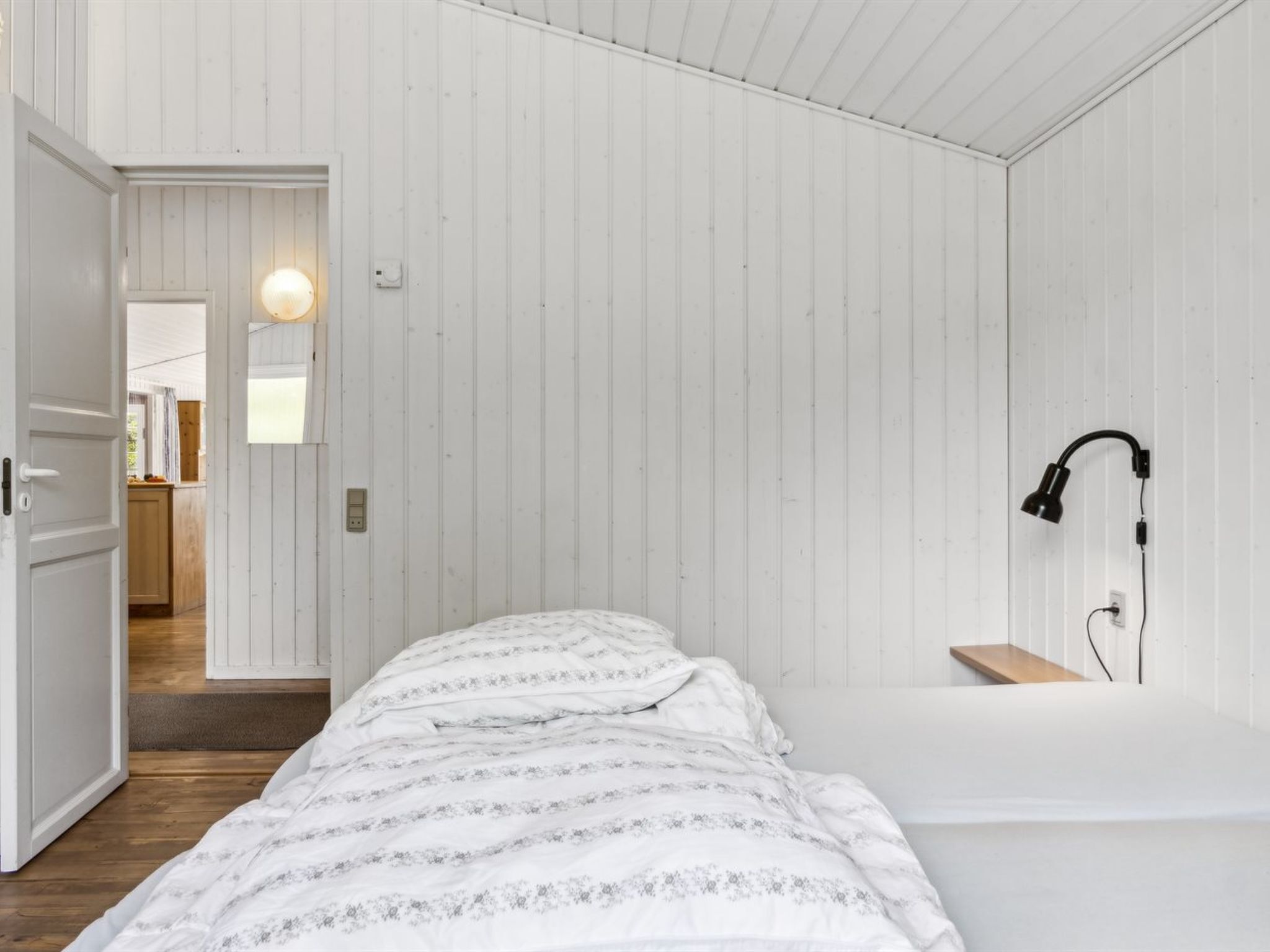 Un dormitorio con cama, lámpara de noche y suelo de madera.