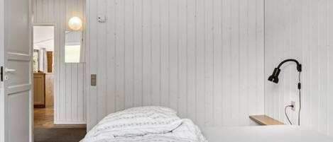Un dormitorio con cama, lámpara de noche y suelo de madera.