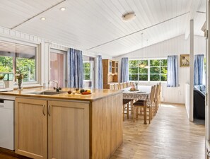 Een ruime keuken met houten kasten, een centraal eiland en een eethoek met een tafel en stoelen.