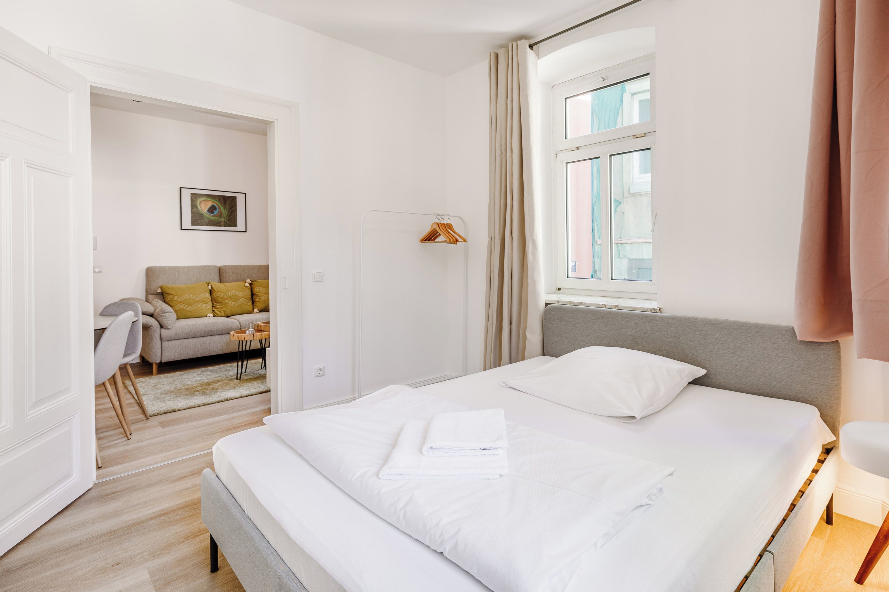 A modern hotel room with a large bed, a bedside table, a window with curtains, and a view of the city.