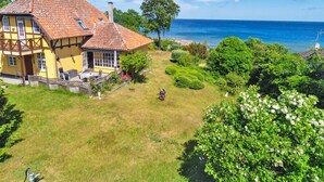 Une maison jaune avec un toit en tuiles, un jardin avec une pelouse et une vue sur la mer.