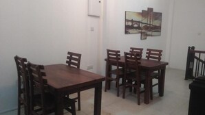Un coin repas avec une table et des chaises en bois, un tableau au mur et une poubelle.