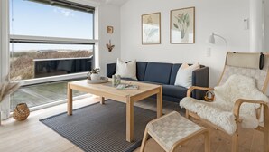 Un salon moderne comprenant un canapé, un fauteuil, une table basse et une grande fenêtre donnant sur l’extérieur.
