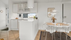 Une cuisine moderne avec des meubles blancs, un îlot central et un coin repas comprenant des chaises et une table, le tout dans des tons blancs.