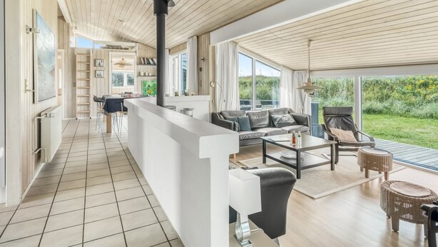 A spacious living area with a high ceiling, a kitchen area, and a large sliding glass door leading to a garden.