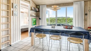 A dining area with a table set for four, a wooden ladder, and a view of greenery outside.