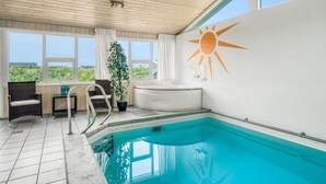 A modern indoor swimming pool with a sun mural, a hot tub, and a view of the greenery outside.