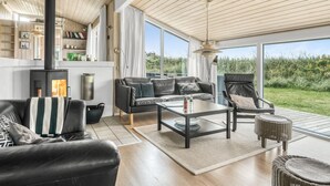 A spacious living room with a large black wood-burning stove, leather sofas, a coffee table, and a view of the outdoors.