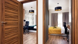 Un dormitorio moderno con puerta de madera, un escritorio con silla, cama con colcha amarilla y lámpara colgante.