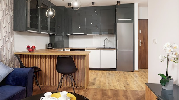 Una cocina moderna con armarios oscuros, encimera de madera y refrigerador de acero inoxidable.