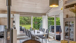 A cozy room with a wood-burning stove, a dining table with chairs, and a view of a lush garden through large windows. - "Anouk" - 2km from the sea by Interhome (Saltum)