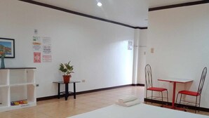A hotel room with a bed, a small table with chairs, a potted plant, and a shelf with shoes. - Wjv Inn Marigondon (Lapu-Lapu)