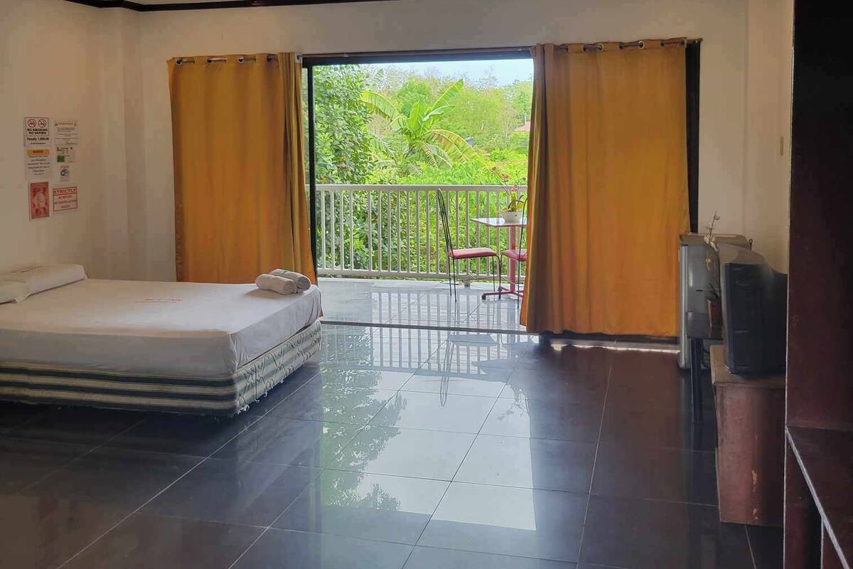 A hotel room with a bed, a TV, and a balcony with curtains.