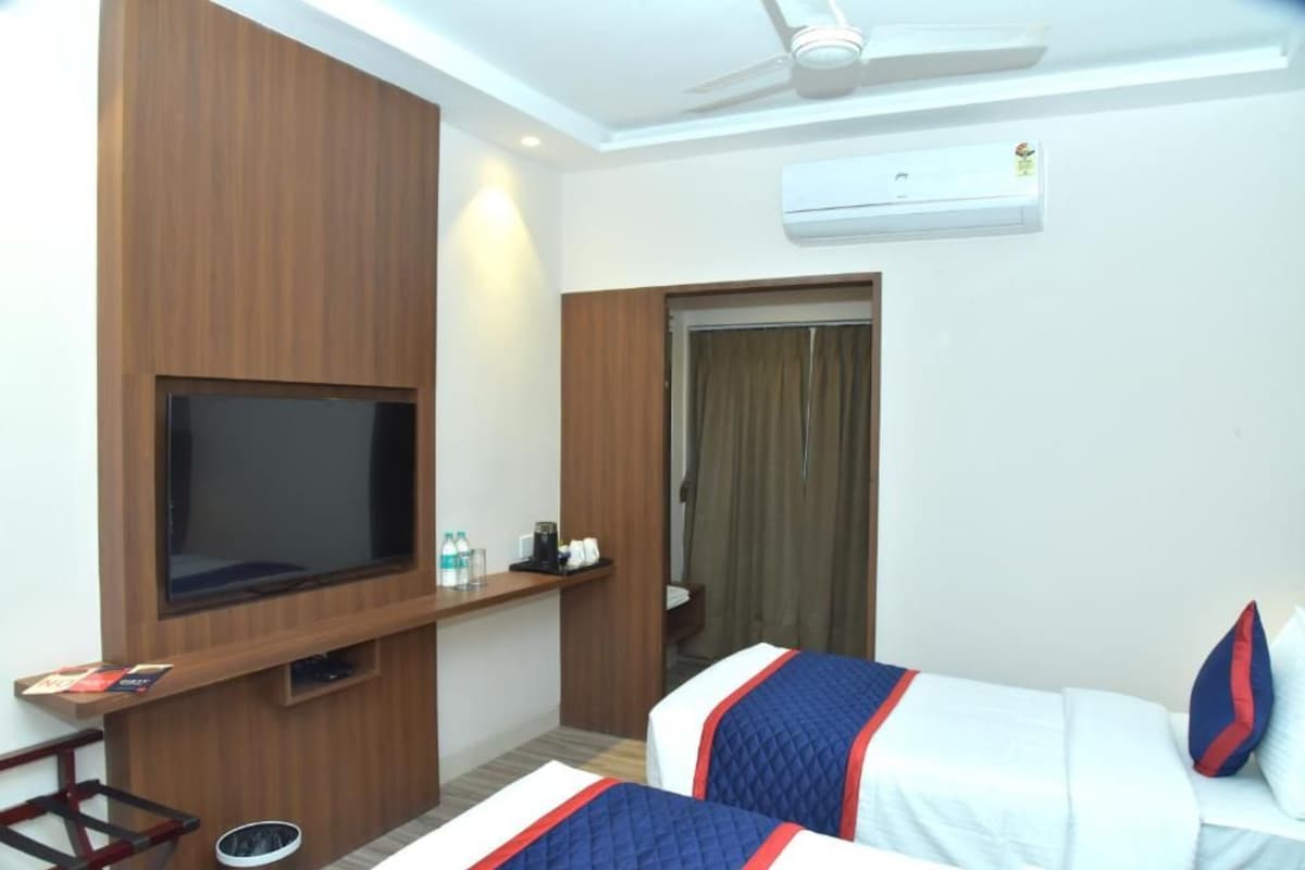 A hotel room with a TV, a bed with a quilted cover, a ceiling fan, and an air conditioning unit.