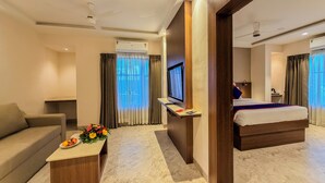 Ein Hotelzimmer mit Bett, einer Couch, einem Fernseher, einem Schreibtisch mit Blumen und einem Fenster mit Vorhängen.