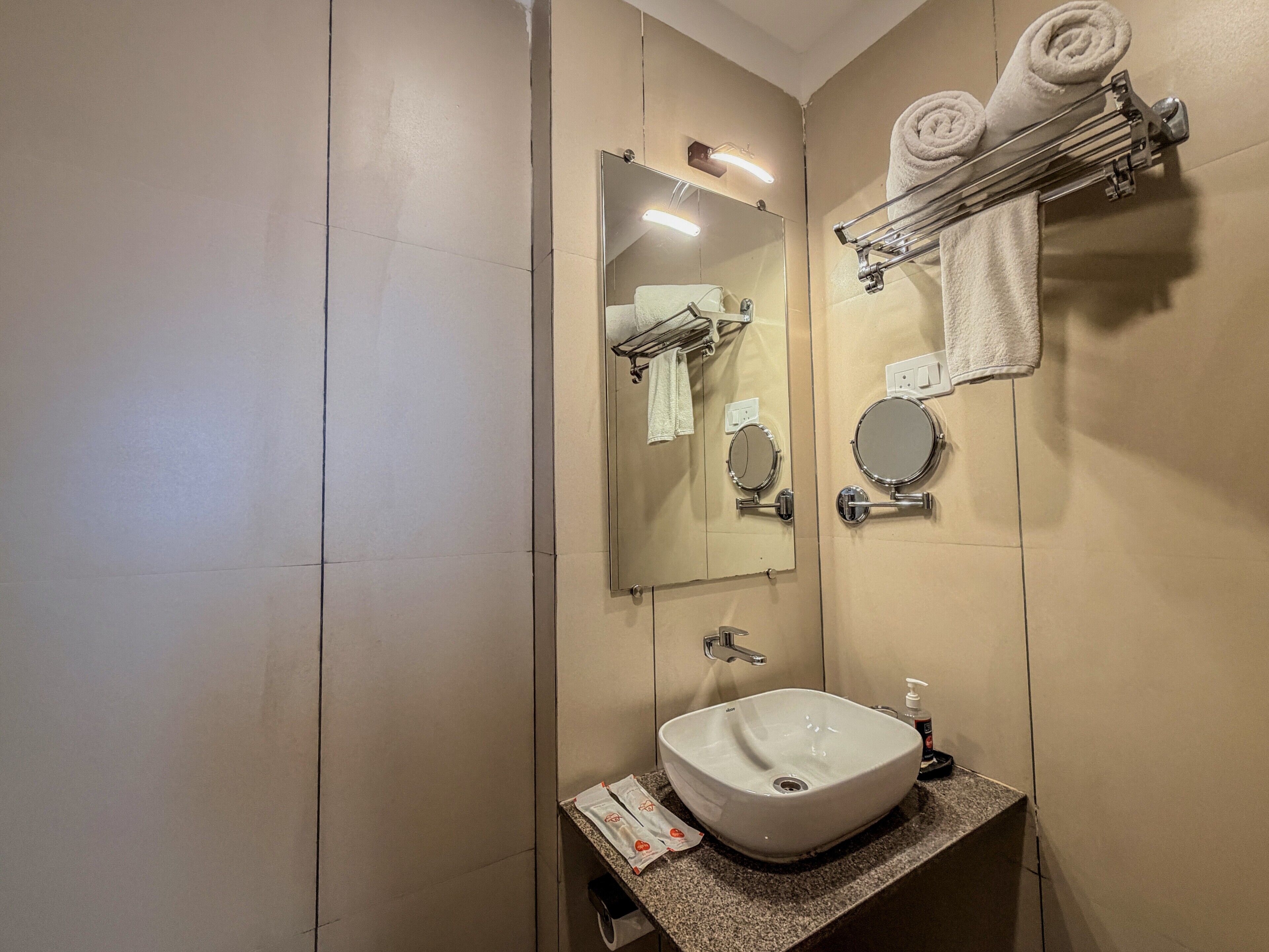 A bathroom with a sink, mirror, towel rack, and a towel dispenser.