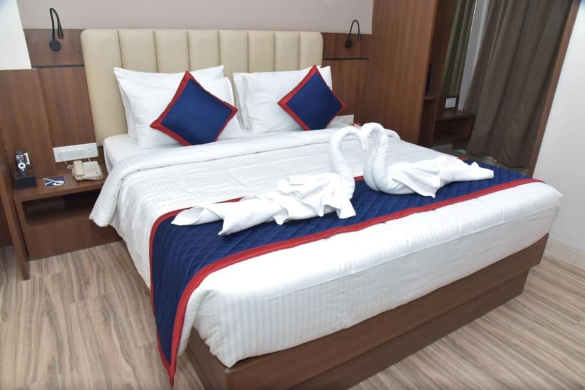 A hotel room with a large bed, a wooden nightstand, a telephone, and a wall-mounted light.