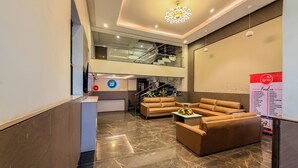 Eine moderne Hotelhalle mit Empfangstresen, Ledersofas, Marmorboden, einer Treppe und einer Kristallleuchtre.'